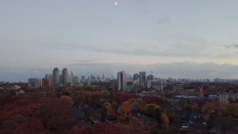 Cinematic-aerial-footage-of-the-skyline-of-Toronto-Canada-with-bright-colored-trees-in-focus,-tilting-up-to-the-moon,-Drone