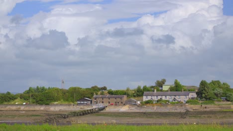 Riverside-cottages-with-slipway,-clouds-racing-behind-and-cloud-shadows-moving-across-frame