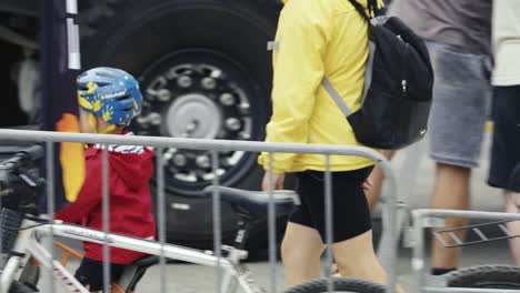 A-little-boy-on-a-bicycle-with-a-helmet-rides-past-cyclists-and-tourists-in-a-parking-lot