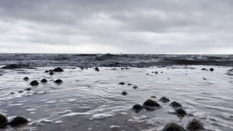 Low-seascape-showing-the-waves-flowing-over-the-rocks-with-barnacles,-on-a-grey-cloudy-day