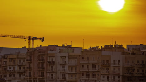 Timelapse-of-Gzira,-Malta-at-sunset-over-many-apartment-buildings-and-a-construction-crane-erected-at-a-new-building