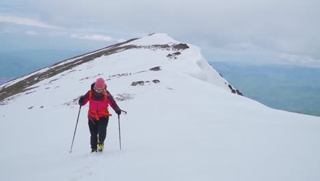 Woman-trekking-through-snow-on-mountain-top-with-ski-poles
