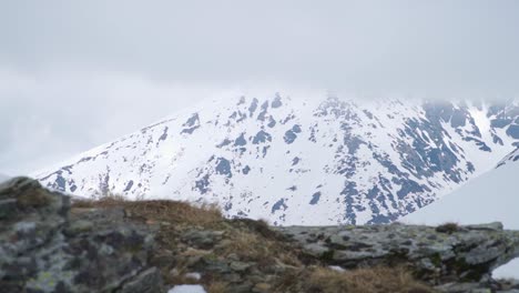 Felsiges-Berggelände-Im-Vordergrund-Und-Schneebedeckte-Klippen-Und-Gipfel-Im-Hintergrund