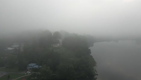 Foggy-morning-aerial-over-still-water-to-white-cross-on-lake-side-hill