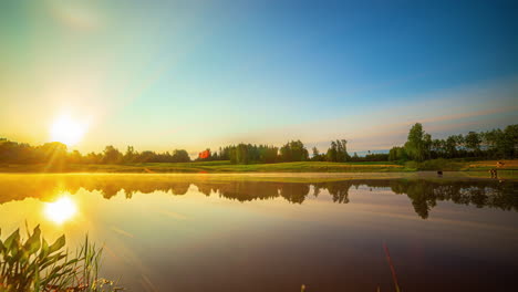 Timelapse-shot-of-sun-rising-over-green-grasslands-along-lakeside-during-morning-time