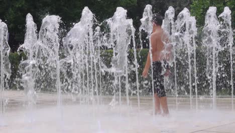 Slow-motion-shot-of-boys-walking-and-running-water-fountains-in-a-city-park