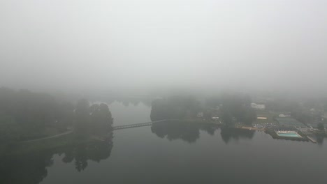Aerial-flyover:-Pedestrian-foot-bridge-on-foggy-rural-lake-on-calm-day