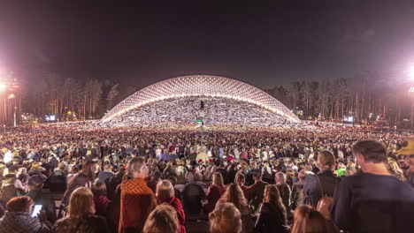 Zeitrafferaufnahme-Einer-Riesigen-Menschenmenge-Von-Einheimischen,-Die-Nach-Sonnenuntergang-Das-Lettische-Gesangs--Und-Tanzfestival-In-Einem-Freiluftstadion-In-Riga,-Lettland,-Genießen