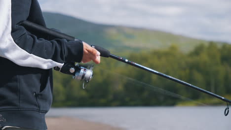 Young-man-spinning-fishing-rod-line-in-Swedish-landscape,-close-up-view