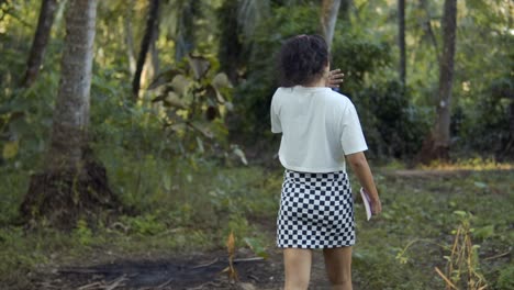 Cinematic-slow-motion-shot-of-a-fashion-model-walking-through-the-forest-in-Goa,-India-in-a-chess-patterned-skirt-and-a-white-shirt