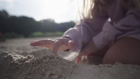 Hände-Eines-Blonden-Mädchens,-Das-Bei-Sonnenuntergang-Eine-Sandburg-Am-Strand-Modelliert
