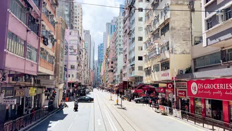 Driving-Down-Des-Voeux-Road-West-in-Sai-Ying-Pun,-Hong-Kong-on-a-Sunny-Day