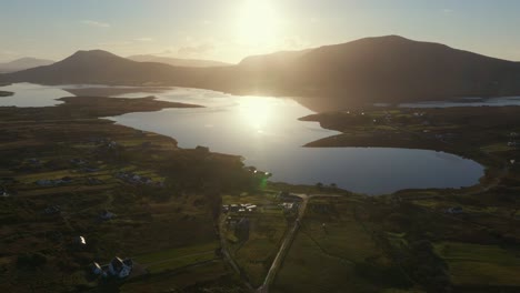 Drone-shot-of-a-small-village-on-Achill-Island-during-sunrise,-showing-grass-fields-and-the-sea