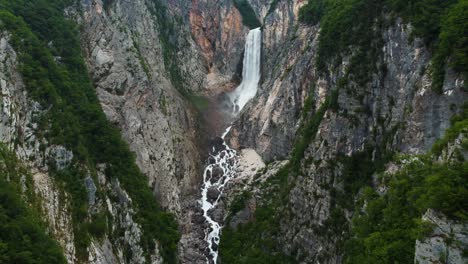 Cinematic-drone-backwards-flight-showing-crashing-Boka-Waterfall-between-steep-cliffs-near-Triglav-National,-Slovenia