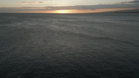 Sunset-aerial-descends-to-sea-water,-wind-blowing-on-ocean-surface