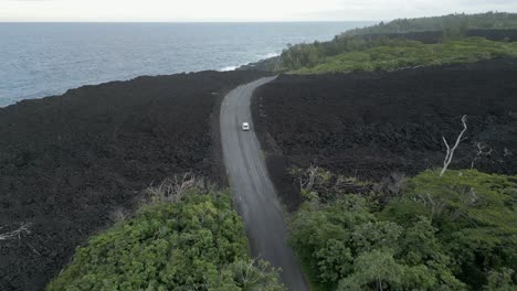 Aerial-tracks-car-driving-on-new-road-over-steaming-black-lava-flow