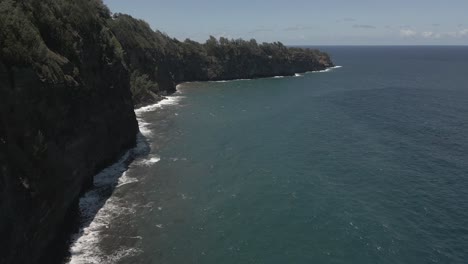 Ocean-aerial-flies-along-tall-rock-cliffs-on-tropical-jungle-coast