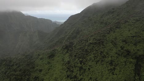 Mountain-fog-aerial-flies-over-hikers-descending-ridge-trail-on-Oahu