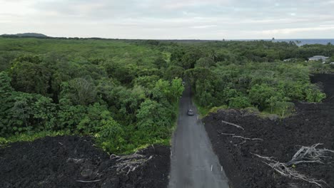 Low-aerial-follows-car-from-new-lava-flow-road-into-dense-coast-jungle