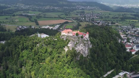 Filmische-Drohnenaufnahme-Des-Schlossbaus-Auf-Einem-Grünen-Hügel-In-Der-Stadt-Bled,-An-Bewölkten-Und-Sonnigen-Tagen,-Slowenien-–-Aufnahme-Im-Orbit