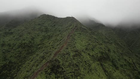 Aerial-flies-down-steep-ridge-trail-to-hiker-in-mountain-fog-on-Hawaii
