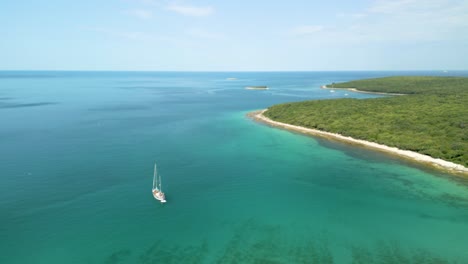 Aerial-footage-of-a-white-sailboat-in-the-calm-Mediterranean-sea-in-front-of-a-paradise-island-with-turquoise-blue-sea-and-lush-green-vegetation-drone-croatia
