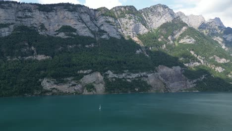 Riesige-Felsige-Berge-Der-Schweizer-Alpen-Schmücken-Den-Walensee,-Während-Eine-Einsame-Yacht-Vorbeisegelt