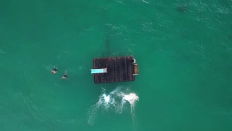 Top-view-of-people-jumping-off-a-floating-platform-at-Coogee-Beach-in-Perth,-Australia