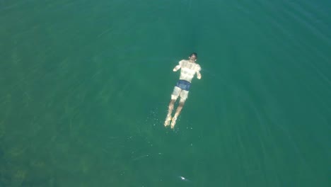 Top-down-drone-footage-of-a-man-swimming-in-a-blue-lake-in-the-mountains