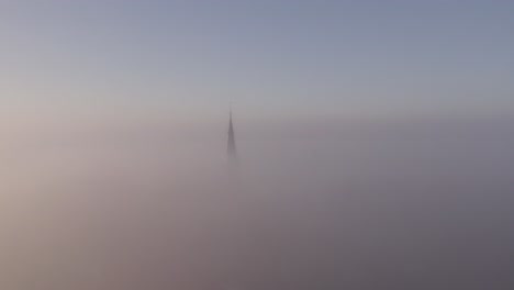 Flying-towards-cornwerd-church-in-Friesland-with-dense-fog,-aerial