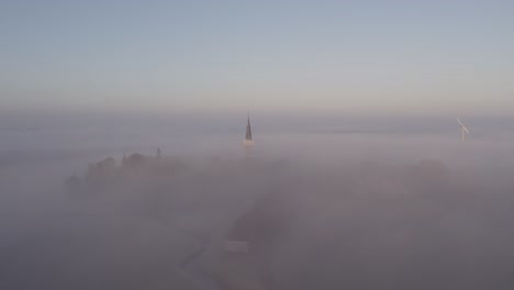 Low-morning-fog-at-cornwerd-with-church-sticking-out-of-the-clouds,-aerial