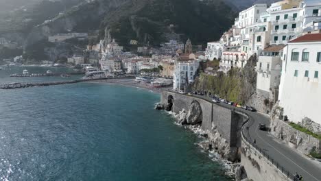 Drone-reveal-of-Italy-Amalfi-village-with-ocean,-cars,-fort-and-beach