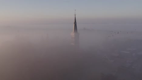 Cornwerder-church-at-province-Friesland-in-dense-morning-fog,-aerial