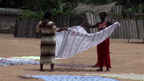 Mujeres-Doblando-La-Ropa-En-La-Playa.-Nigeria