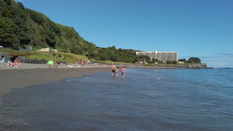 People-on-vacation-at-the-beach-of-Agua-de-Alto-with-Pestana-Bahia-Praia-Hotel-in-the-background-on-a-sunny-summer-day,-San-Miguel-Island,-Azores,-Portugal---July-2023