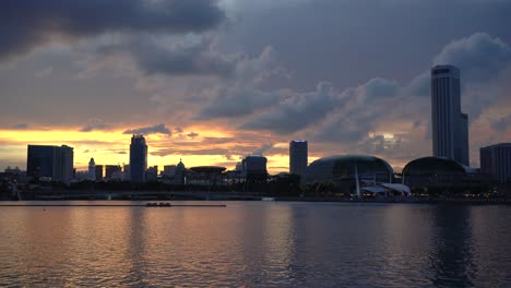 Herrlicher-Blick-Auf-Den-Sonnenuntergang-Mit-Einem-Ruhigen-Fluss,-Der-Von-Der-Modernen-Architektur-Der-Marina-Bay,-Den-Wolkenkratzern-Singapurs,-Abfließt
