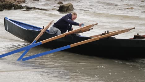Ein-Einzelner-Mann-Arbeitet-An-Der-Rettung,-Um-Wasser-Aus-Einem-Traditionellen-Irischen-Holzboot-Zu-Entfernen