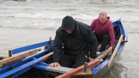 Closeup-of-team-of-people-stretching-wearing-hoodies-sitting-in-currach-boat