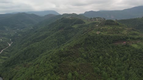 Drone-Ver-Colinas-Y-Montañas-Con-Bosque-Al-Lado-Del-Lago,-Paisaje-Natural-Bajo-El-Cielo-Nublado