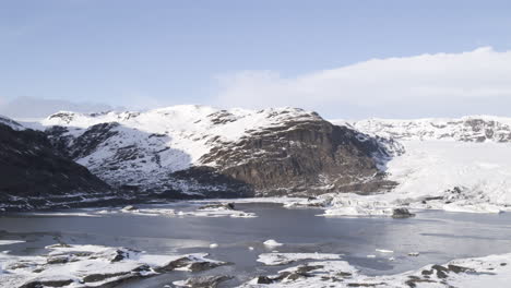Aerial-establishing-shot-of-an-Icelandic-mountain-valley-with-frozen-lake-and-snowy-ground