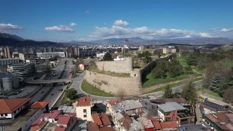 The-castle-in-the-center-of-Skopje-is-among-the-buildings,-flag-waving-in-the-castle-garden