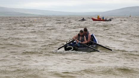 Men-dry-off-oars-and-paddles-of-currach-boat-in-open-water,-preparing-for-race