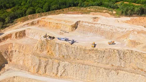 Aerial-View-Of-Diggers,-Excavators,-Dumpers-And-Bulldozers-In-A-Limestone-Quarry---drone-shot