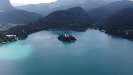 Cinematic-drone-shot-of-bled-island-with-church-and-mountain-range-of-Slovenia-in-background