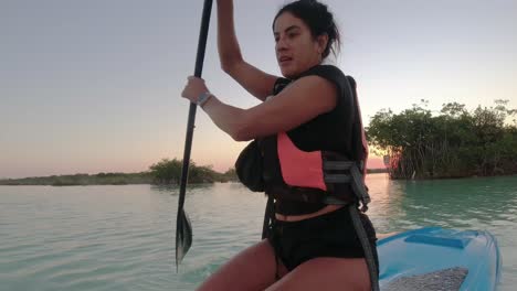 Young-woman-paddling-on-a-SUP-board-in-Bacalar-blue-Lagoon-Mexico-travel-destination-at-sunset,-recreational-holiday-activities