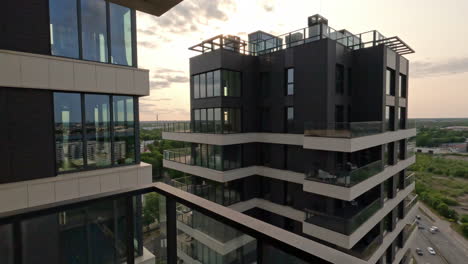 Modern-apartment-building-revealed-behind-glass-railing-at-sunset,-push-in