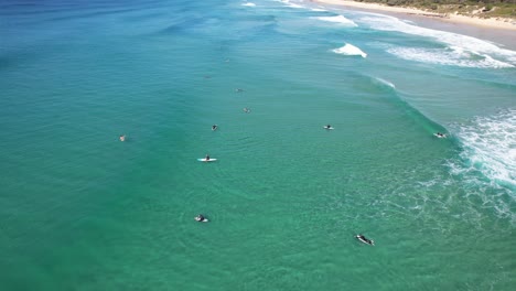 Surfers-Floating-On-The-Turquoise-Seascape-Of-Sunshine-Beach-In-Queensland,-Australia---aerial-drone-shot