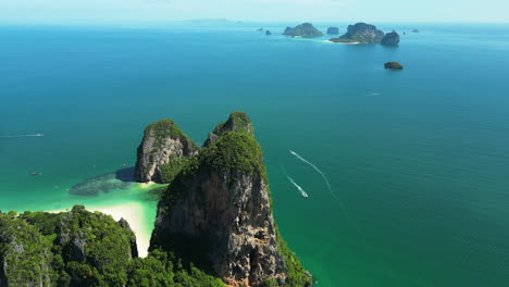 Luftaufnahme-Aus-Der-Umlaufbahn,-Die-Die-Wunderschöne-Landschaft-Thailands-Mit-Booten-Auf-Dem-Meer-Und-Dem-Berühmten-Sandstrand-Von-Railay-An-Einem-Sonnigen-Tag-Zeigt-–-Panoramablick-Mit-Inseln-Im-Hintergrund-–-Paradies-Auf-Erden-–-Von-Oben-Nach-Unten