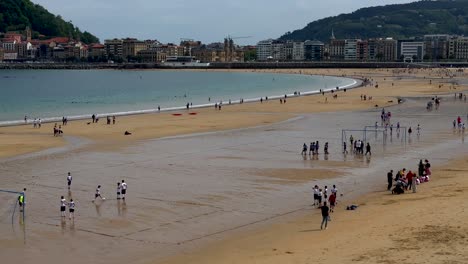 Wide-shot-showing-beach-soccer-school-Tournament-at-sandy-beach-of-San-Sebastian-City-during-ebb-tide---Buildings-and-mountains-in-Background