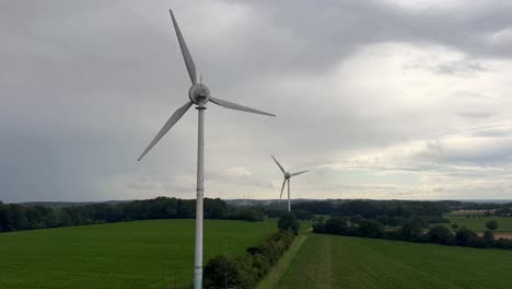 Luftaufnahme-Von-Rotierenden-Windkraftanlagen-Auf-Einer-Grünen-Feldlandschaft-An-Bewölkten-Tagen